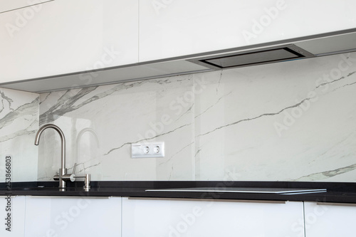 Fotografie White glossy kitchen with black quartz countertop and marble tile backsplash