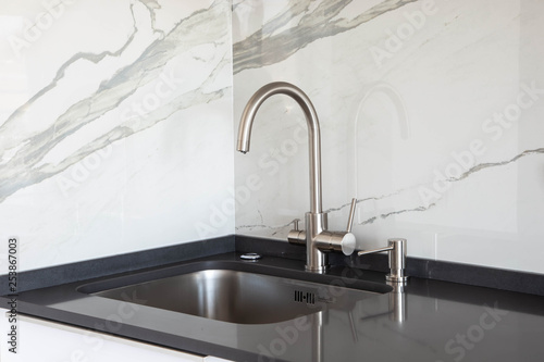 Close up of a undermounted sink and mixer in white and black kitchen design with marble tile backsplash and dark grey quartz countertop. 