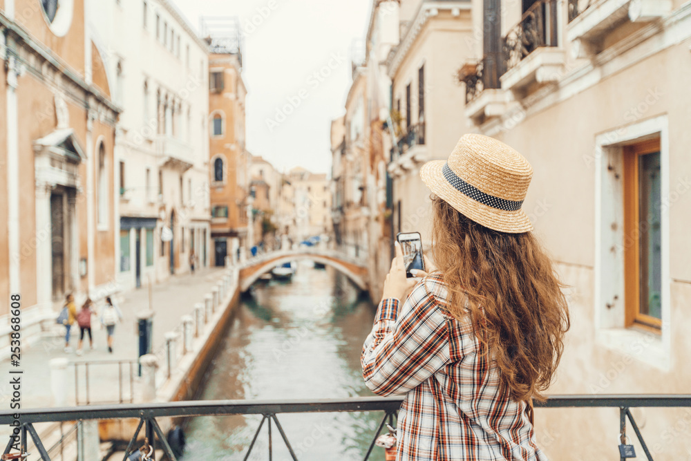 beautiful woman taking a photo on a mobile phone (smartphone) canal in Venice, Italy standing on a bridge
