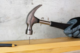 Male hand in a black construction glove hammering a nail with a hammer against the background of a concrete wall.