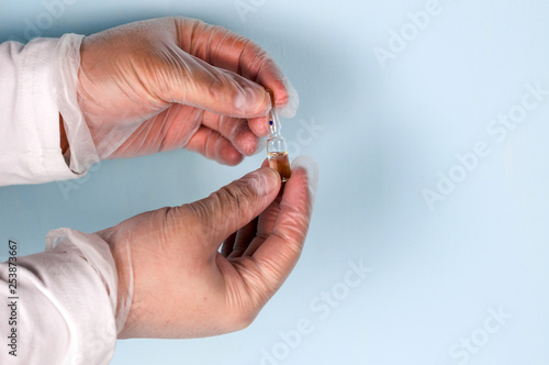 Male hand in a transparent medical nitrile glove holds a vial of medication. Medicine concept