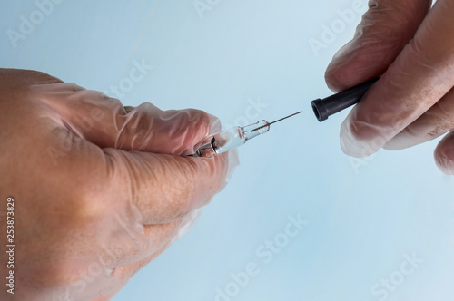 A male hand in a transparent medical nitrile glove holds a small syringe with medicine with a thin needle for subcutaneous administration. The concept of medicine, prevention of thrombophilia. IVF
