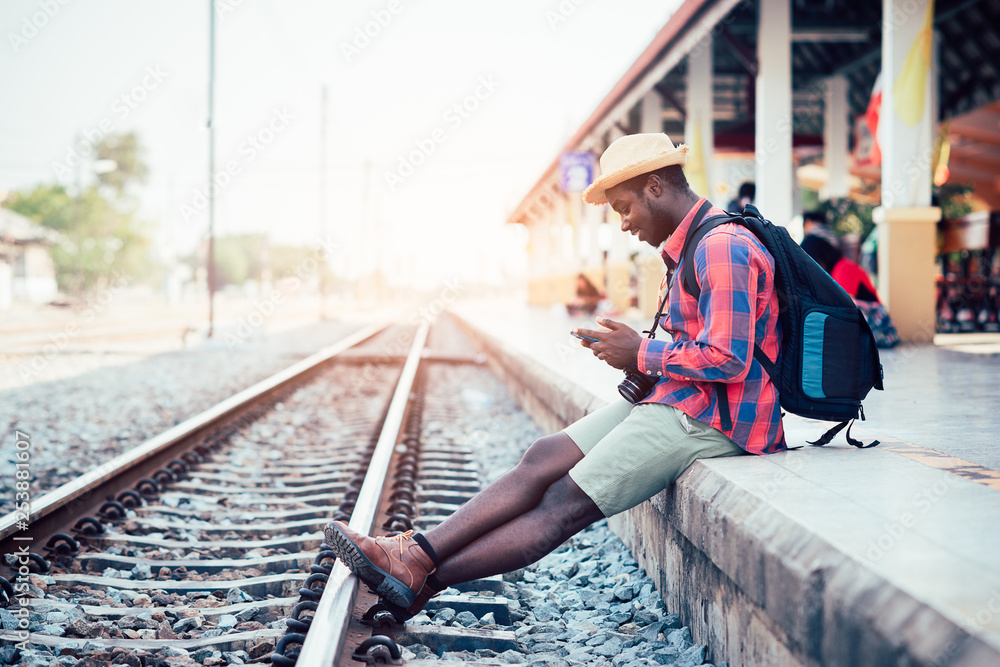 African man traveler playing smartphone waiting for the train on railroad station African man traveler playing smartphone waiting for the train on railroad station