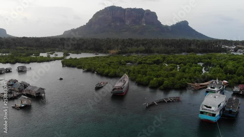 Drone ascending and backing from boats moored near homes on stilts in a peaceful bay near mangroves in Tawi Tawi, the Philippines. Sunset view of a small village on the water. photo