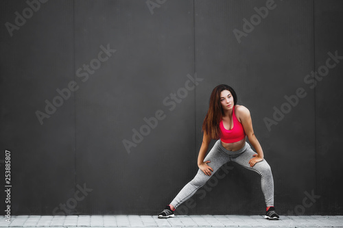 Sport fitness girl in fashion sportswear doing fitness exercise in the street, on gray wall background ,outdoor sports. Urban style.