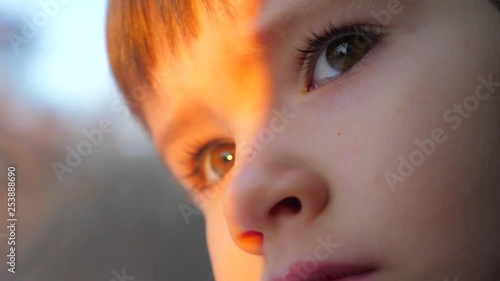Sun light on the face of passenger. Close-up shot of a little curious boy looking out of the window in train. Child reflecting in the glass. The boy looks at sun. Facial emotions of little traveler.