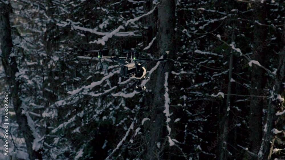 Slow motion of a black drone blending into its environment in the dark snowy forest, 23.98 fps. Slow motion of a black drone blending into its environment in the dark snowy forest, 23.98 fps.