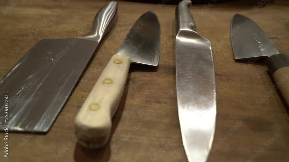 Dolly shot left to right showing various sharp, large kitchen knives on a rustic wooden table