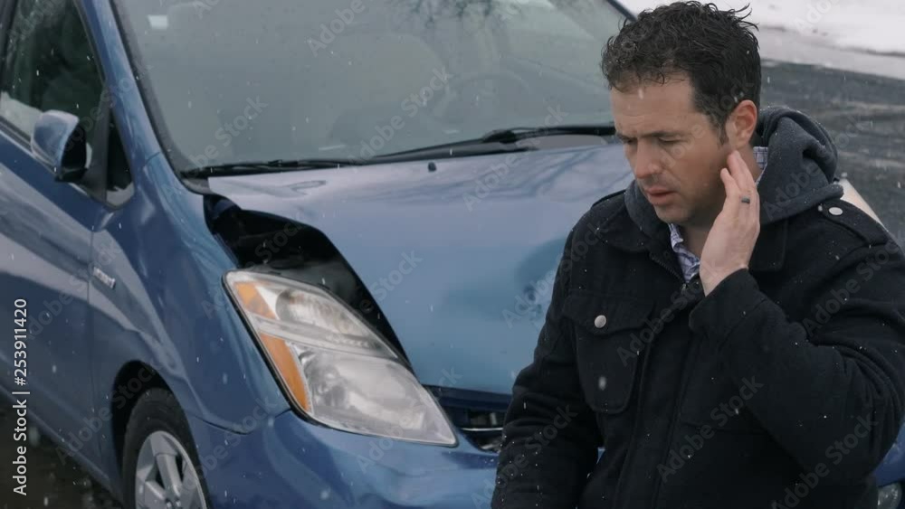 Camera remains fixed as man stands in front of wrecked car rubbing his neck in pain Camera remains fixed as man stands in front of wrecked car rubbing his neck in pain