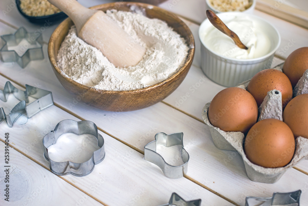 Оat flour in a wooden bowl with a spoon in the middle of the table, next to baking ingredients and forms for cookies. Culinary background Оat flour in a wooden bowl with a spoon in the middle of the table, next to baking ingredients and forms for cookies. Culinary background