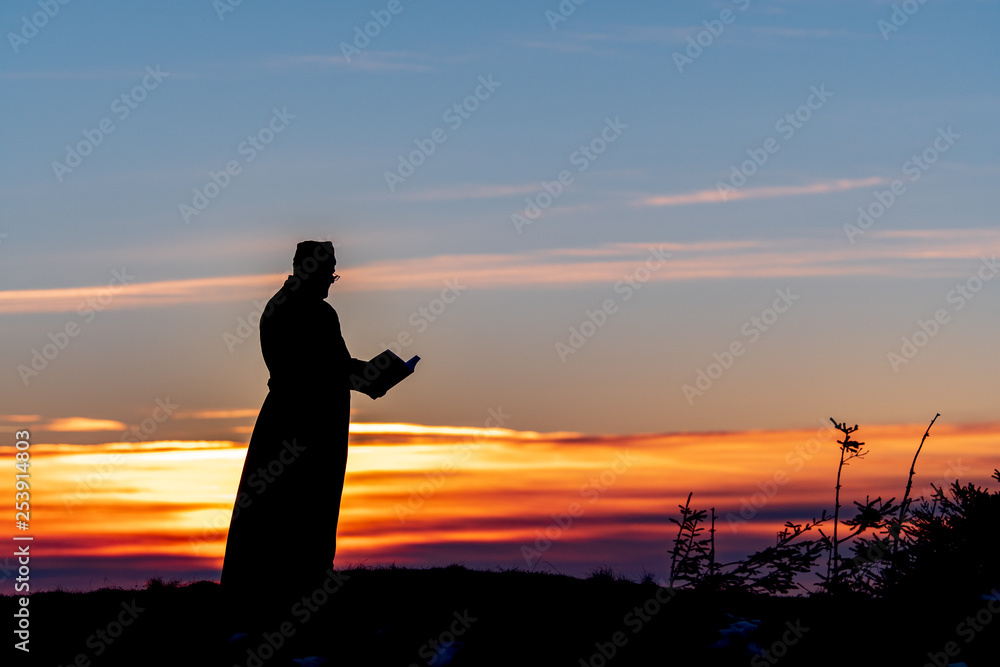 Priest silhoute reading in the sunset light, Romania