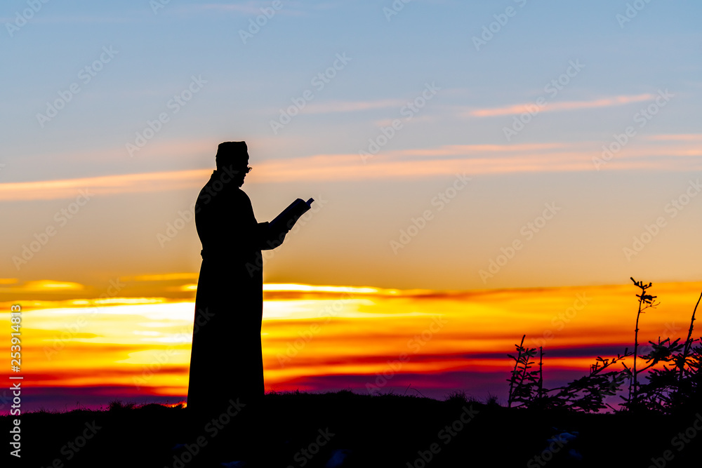 Fototapeta premium Priest silhoute reading in the sunset light, Romania
