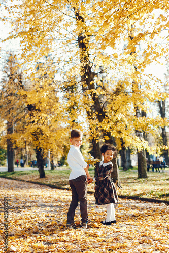 little beautiful dark-skinned girl walks in the autumn park with her European little friend