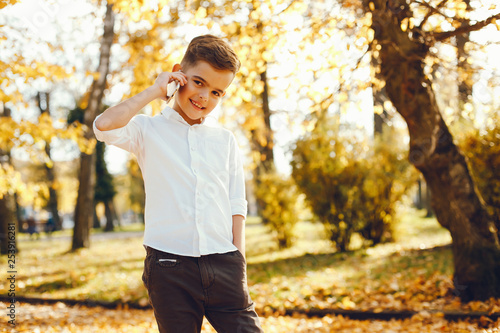 little cute boy in a white shirt standing in a autumn park with phine photo