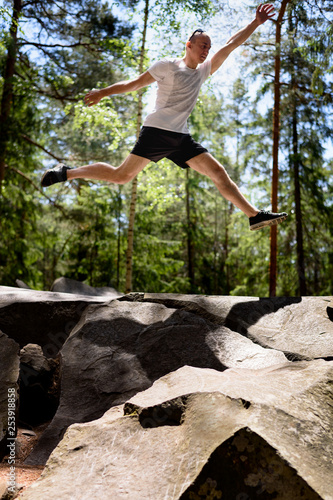 Young man jumps on a rock in a coniferous forest. Active extreme tourism