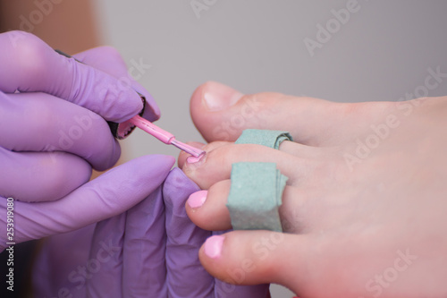 Covering toenails with pink nail polish. Close-up. Manicure salon