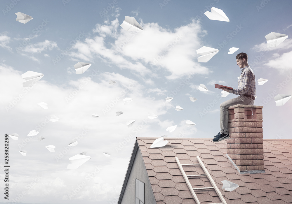 Man on brick roof reading book and paper planes flying in air Man on brick roof reading book and paper planes flying in air