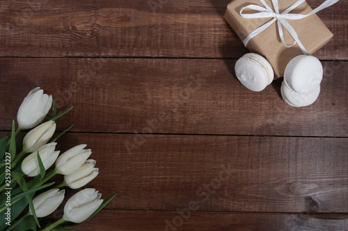 Bunch of white tulips, macaroons and gift box on brown wooden table. Greeting concept. White ribbon, women or mothers day, springtime
