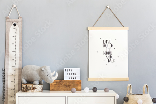 Stylish and cute scandinavian decor of child room with mock up poster, white shelf, natural toys, hanging kid measure basket for accessories and teddy bears. Minimalistic concept of interior.