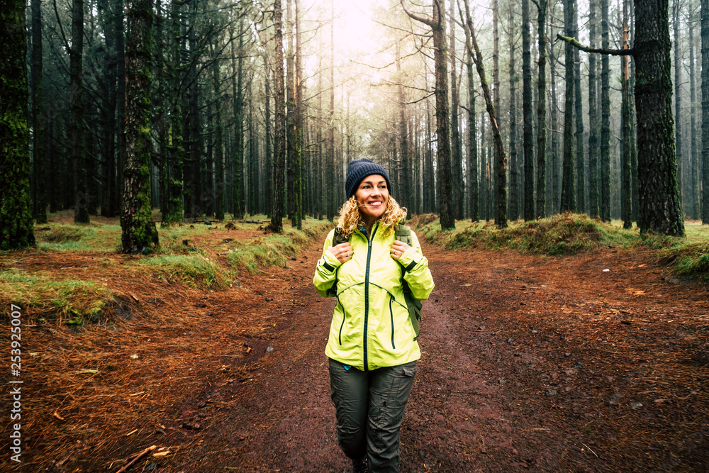 Happy hiker caucasian woman smile and enjoy the nature walking in a forest with high trees - alternative outdoor leisure activity and vacation lifestyle - sun in backlight and mist concept