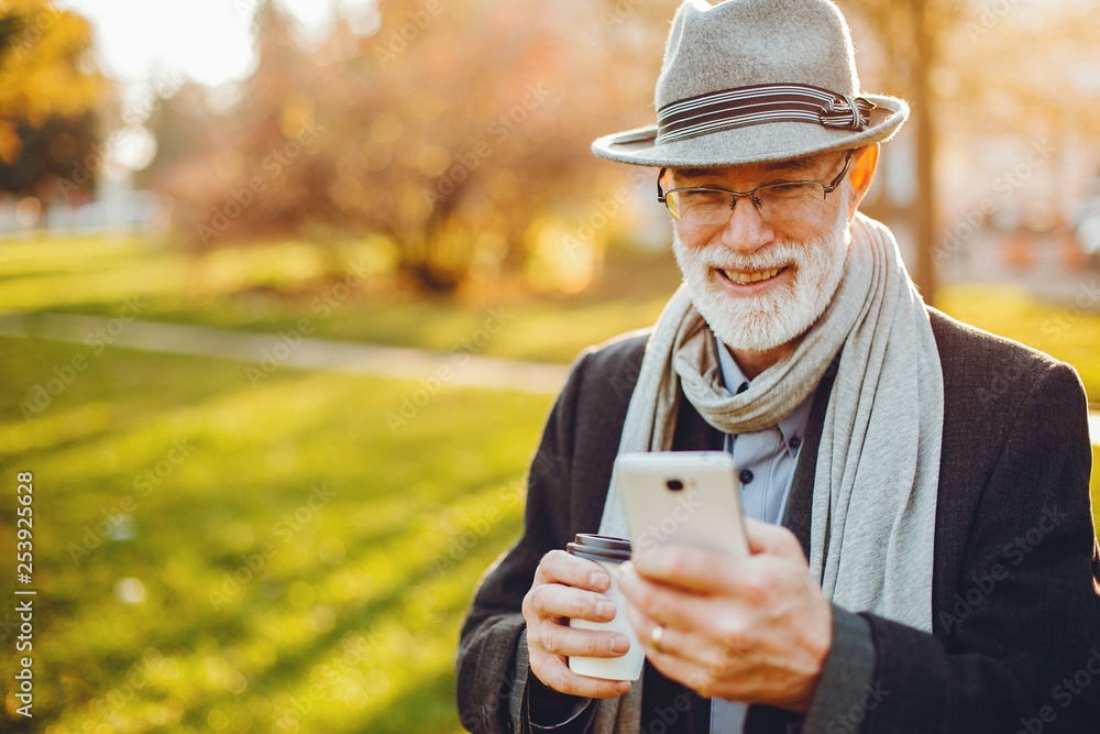 Handsome grandfather in a autumn park. Old man in a gray jacket and hat. Male with coffee Handsome grandfather in a autumn park. Old man in a gray jacket and hat. Male with coffee