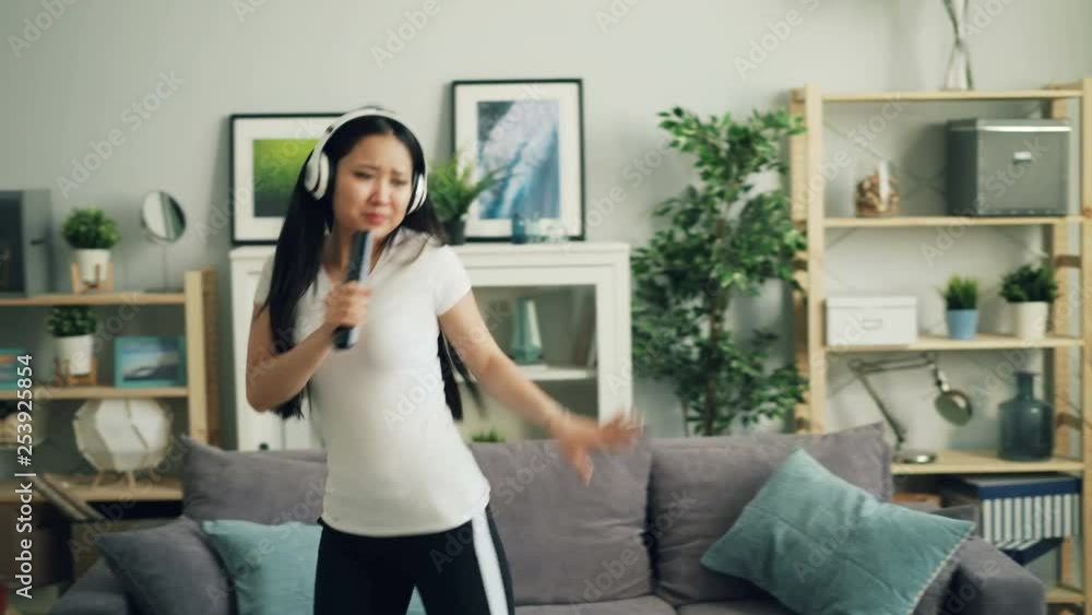 Playful mixed race girl is singing in remote control and dancing at home listening to music in headphones having fun enjoying free time activity. Youth and leisure concept. Playful mixed race girl is singing in remote control and dancing at home listening to music in headphones having fun enjoying free time activity. Youth and leisure concept.