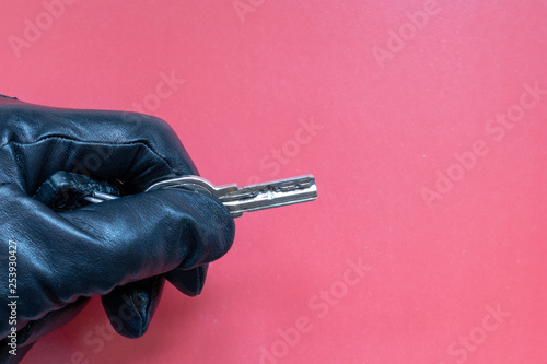 Key in hand in leather glove on pink background.