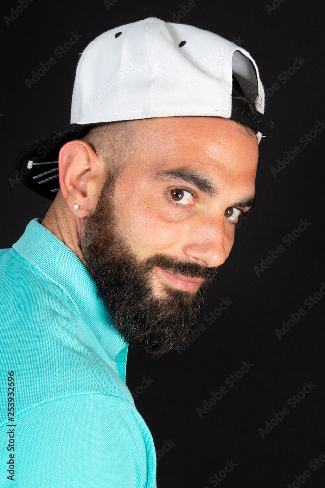 Portrait of young beautiful arab man with cap posing and looking camera in studio shot on black background