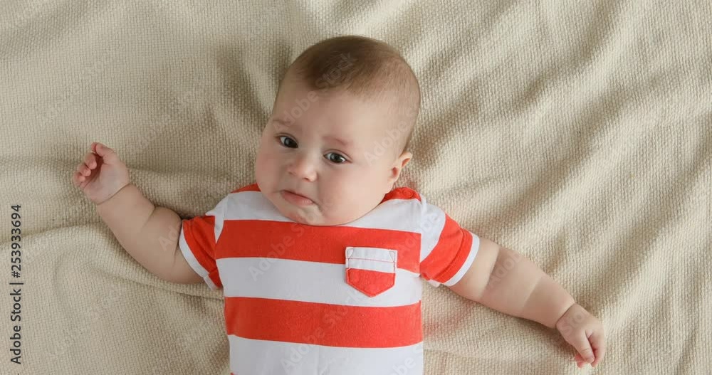 Top view portrait of baby start to cry, lying on the bed and call mother. Live facial