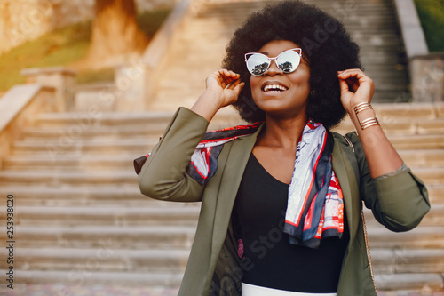 Fashionable girl in a summer city. Black lady in a green jacket. Woman in a red scarf. Famale with sunglasses
