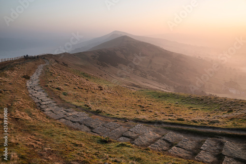 Stunning Winter sunrise landscape image of The Great Ridge in the Peak Distrit in England with a cloud inversion and mist in the Hope Valley with a lovely orange glow