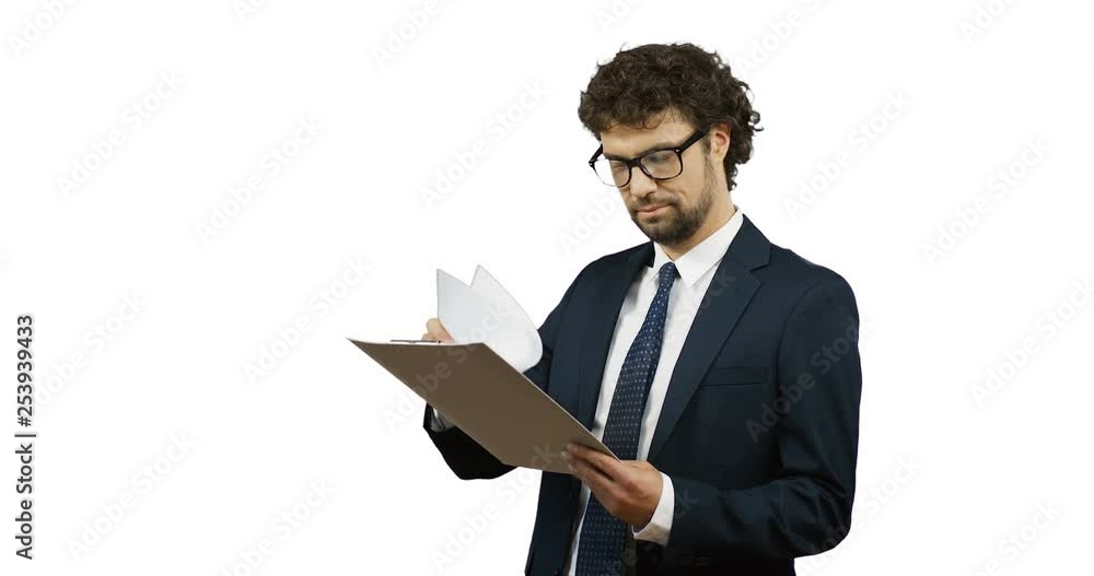 Handsome Caucasian man in the glasses, suit and tie looking at the documents in his hands and doing yes gesture with his hand to the camera on the white back screen. Handsome Caucasian man in the glasses, suit and tie looking at the documents in his hands and doing yes gesture with his hand to the camera on the white back screen.