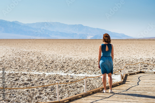 Young woman wearing a blue dress is enjoying the view in Badwater basin in Death Valley National Park, California in United States of America. © blazekg