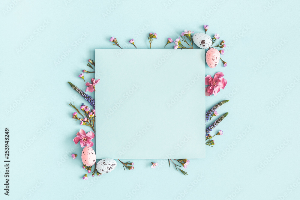 Easter composition. Easter eggs, flowers, paper blank on pastel blue background. Flat lay, top view, copy space