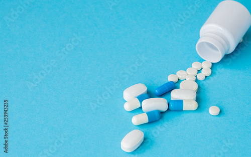 Close up pills spilling out of pill bottle on blue background. Medicine, medical insurance or pharmacy concept