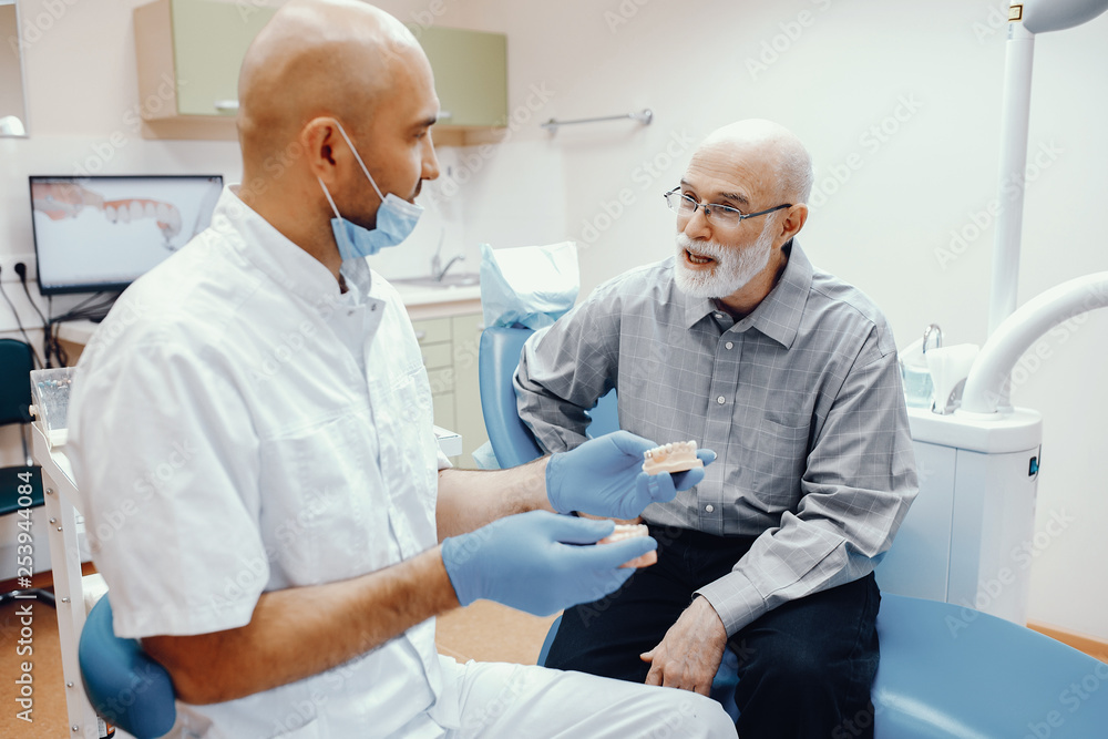 Handsome old man talking to the dendist. Two men in the dentist's office. The doctor shows the patient dentures Handsome old man talking to the dendist. Two men in the dentist's office. The doctor shows the patient dentures