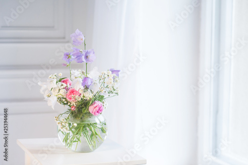 Bedside table, vase with rose and lilac flowers. White background. Copy space