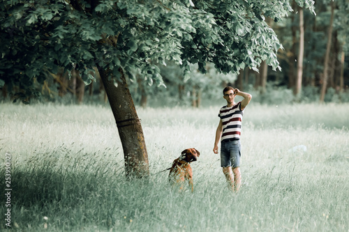 young man with his dog standing near a tree in the Park.