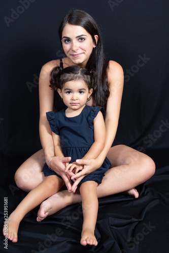 Mother sitting with her daughter under black floor wall studio background