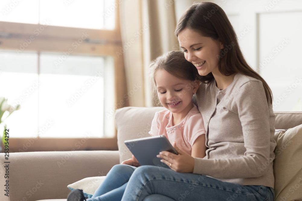 Happy mom and kid daughter using digital tablet on sofa Happy mom and kid daughter using digital tablet on sofa