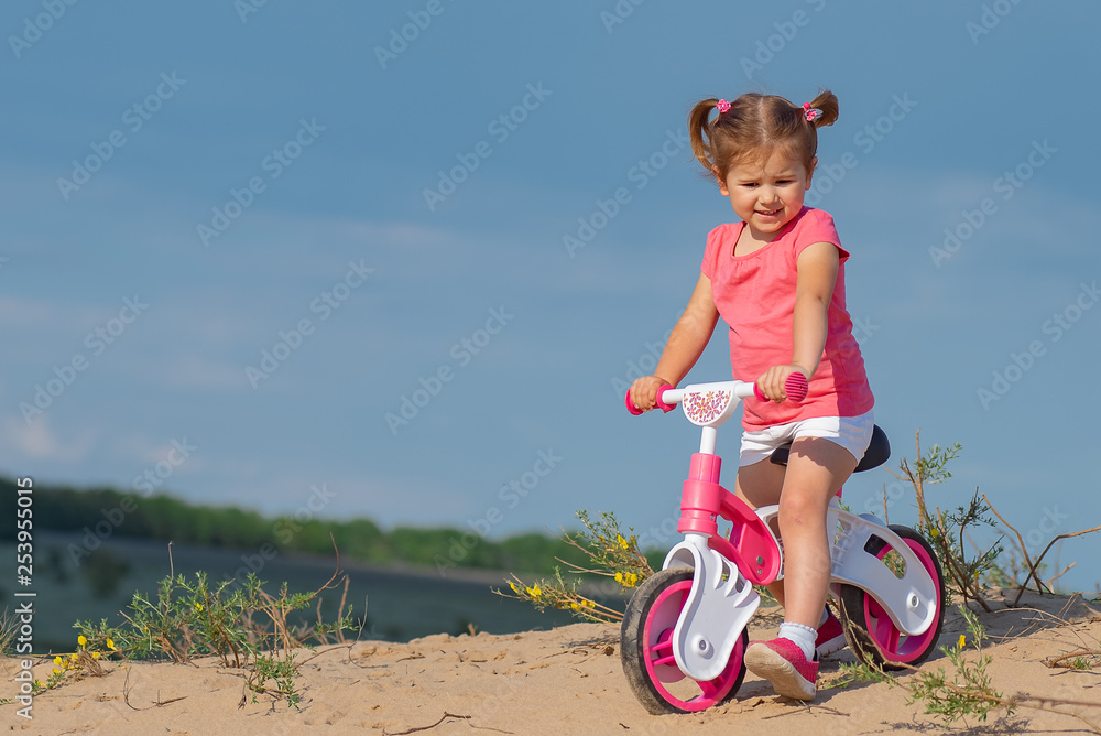 Hello spring, laughter and joy. Baby sport. Overcoming difficulties and new routes. Baby girl riding on pink bicycle in the city park for children.Text place, copyspace