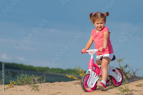Fototapeta Naklejka Na Ścianę i Meble -  Hello spring, laughter and joy. Baby sport. Overcoming difficulties and new routes. Baby girl riding on pink bicycle in the city park for children.Text place, copyspace