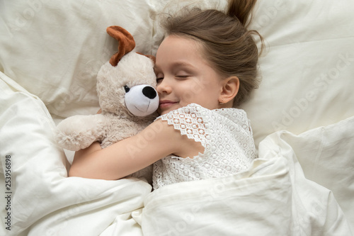 Cute little kid girl hugging teddy bear sleeping in bed