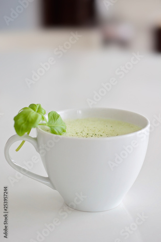 Healthy green tea matcha latte with soy and oat milk in a white tea cup decorated with basil and foam on top - a warm beverage to boost brain function and as a cancer prevention!