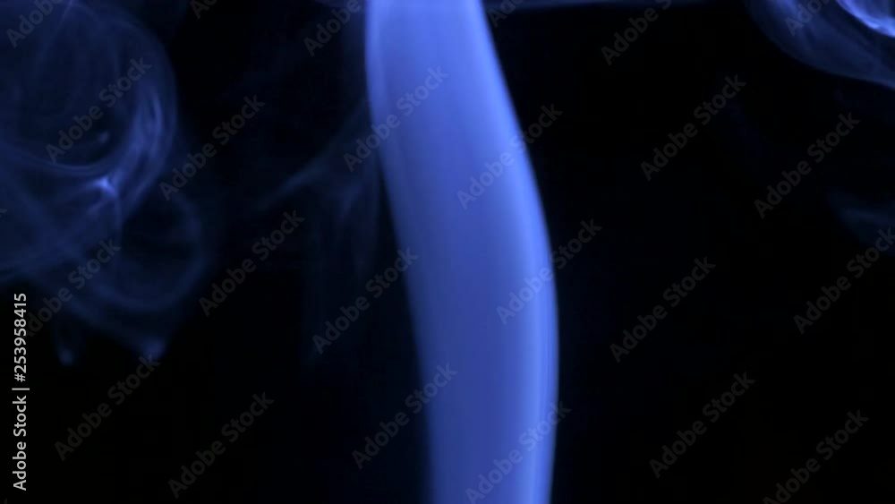 Thin trickle of bright neon blue smoke slowly rising graceful twists up on black background. Colored smoke blowing from bottom to top. Closeup Thin trickle of bright neon blue smoke slowly rising graceful twists up on black background. Colored smoke blowing from bottom to top. Closeup