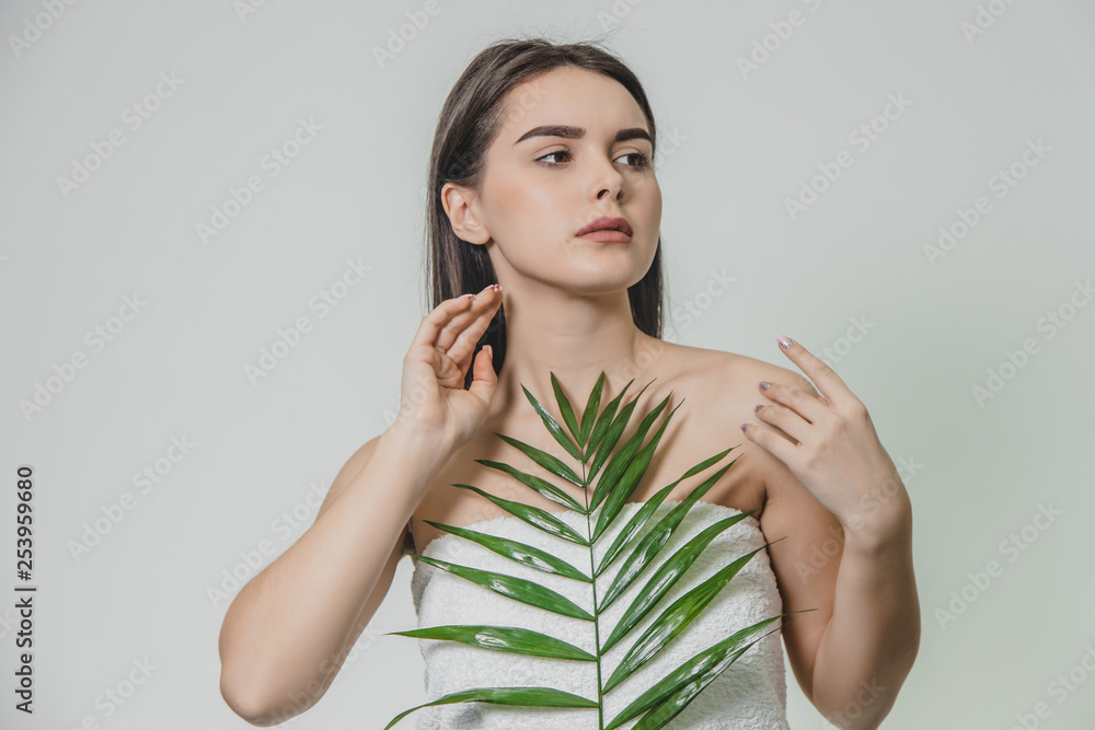 Beautiful young woman with perfect skin and natural make up posing on a white background with ferns. Young fashion model with long hair care for her face and body. Beautiful young woman with perfect skin and natural make up posing on a white background with ferns. Young fashion model with long hair care for her face and body.