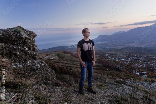 Portrait in growth.. Young attractive man  standing on the top of mountains looks into the distance at Violet sunset.  © Eno1