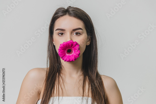Beautiful young girl standing on a white background. During this time, it holds the flower's mouth. © Andrii