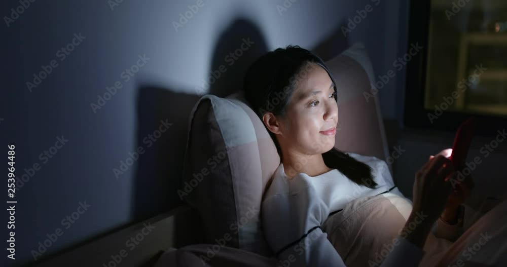 Woman use of mobile phone and lying down on bed at night Woman use of mobile phone and lying down on bed at night