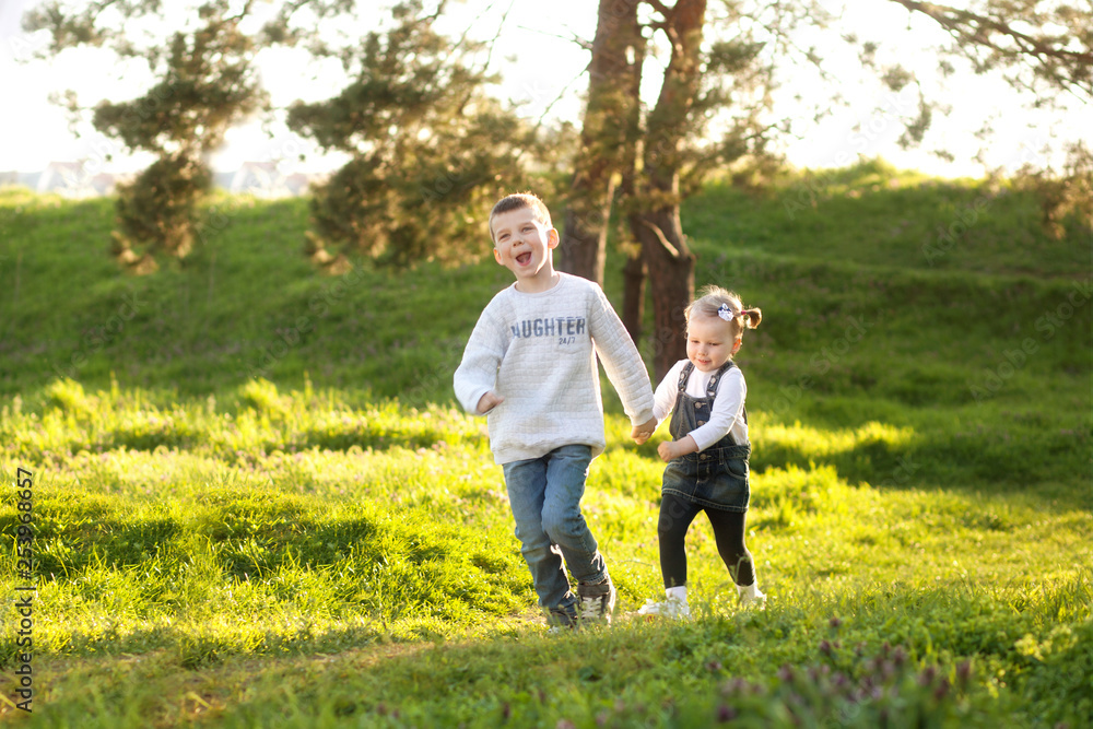Fototapeta premium Cute children boy and girl friends running through the park in spring on a sunny day.